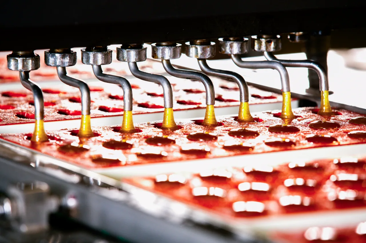 Machine doseert rode pâte de fruits-massa in mallen op de productielijn
