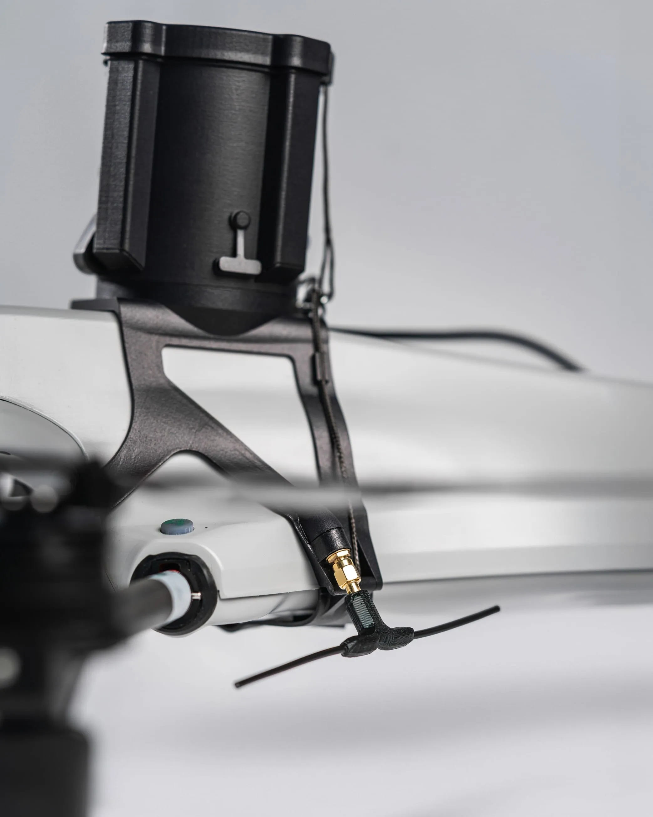 Close-up of a drone's mounted electronic component and antenna on its white arm.