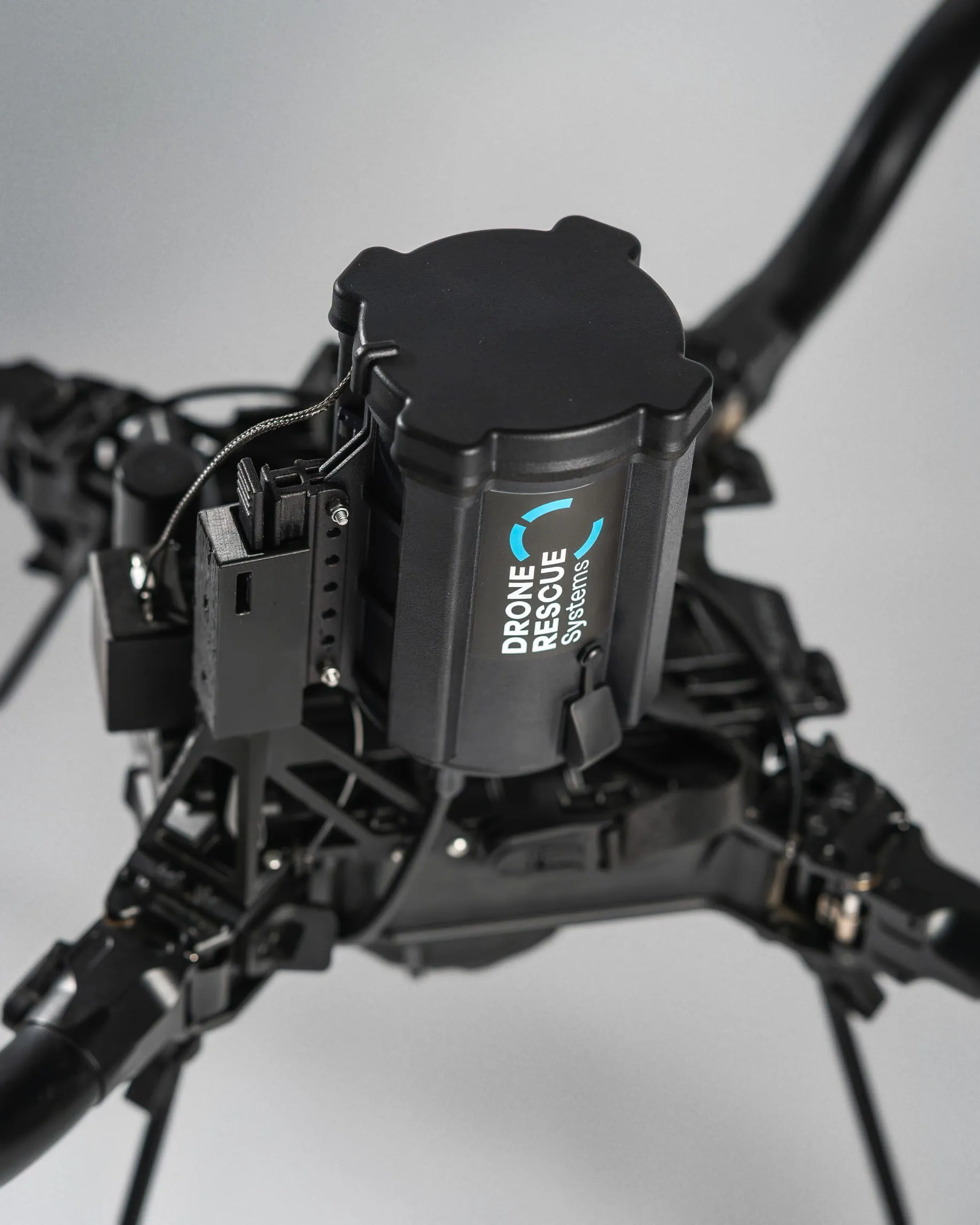 Close-up of a black drone component labeled Drone Rescue Systems on a gray background.