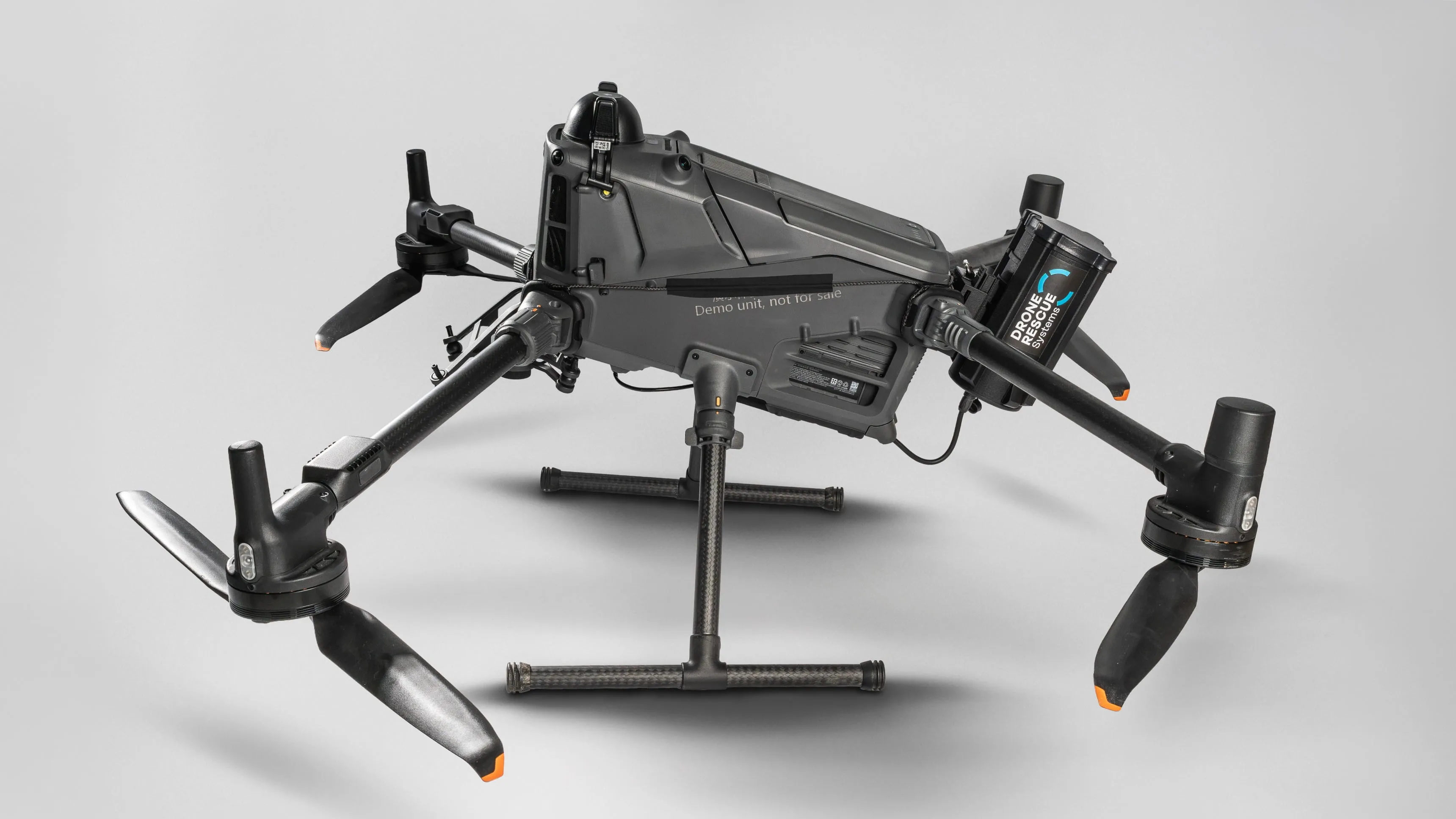 Black quadcopter drone with four propellers and a mounted Rescue Systems cylinder on gray background.