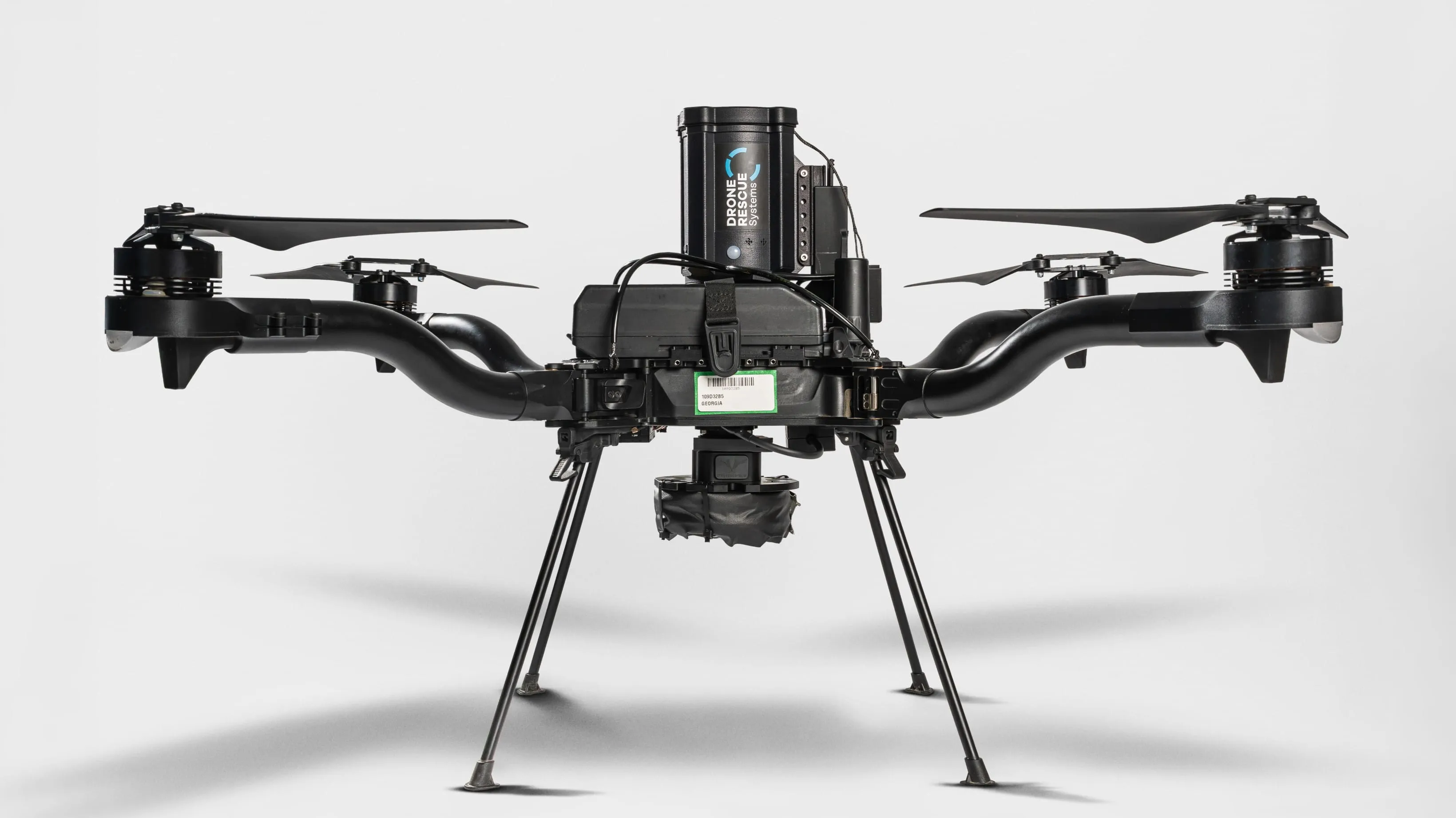 Black quadcopter drone with curved arms and landing legs on a white background.