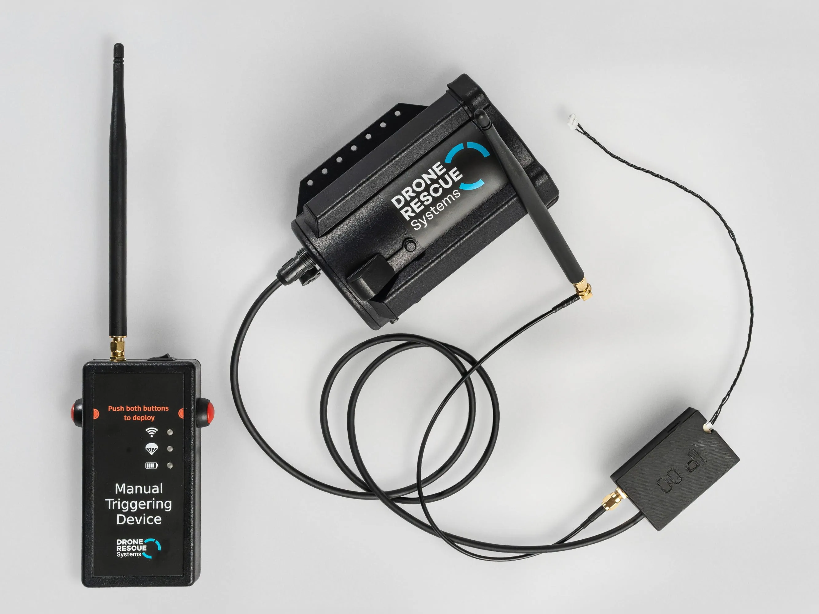 Black wireless manual triggering device and connected drone rescue system components with antennas on a gray surface.