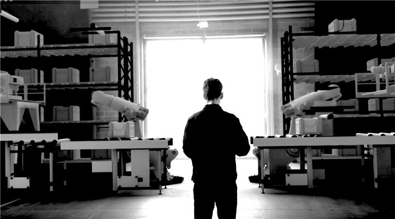 A lone worker walking through a working factory toward daylight, with machinery and shelving on either side