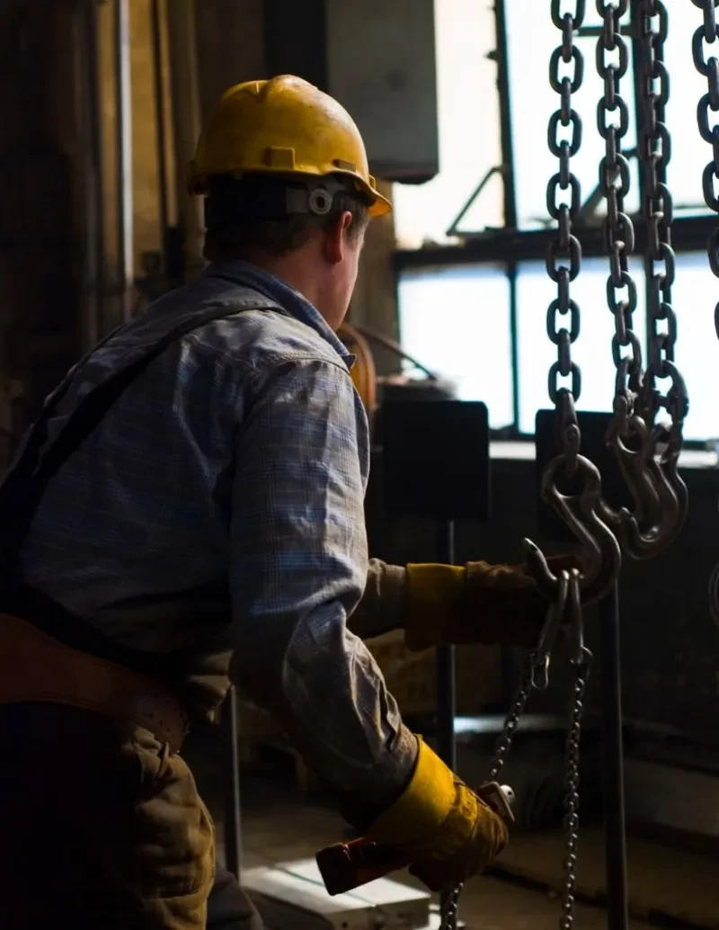 Industrial worker in a hard hat and gloves operating heavy chain lifting equipment in a warehouse, representing workplace personal injury cases in Missoula, Montana