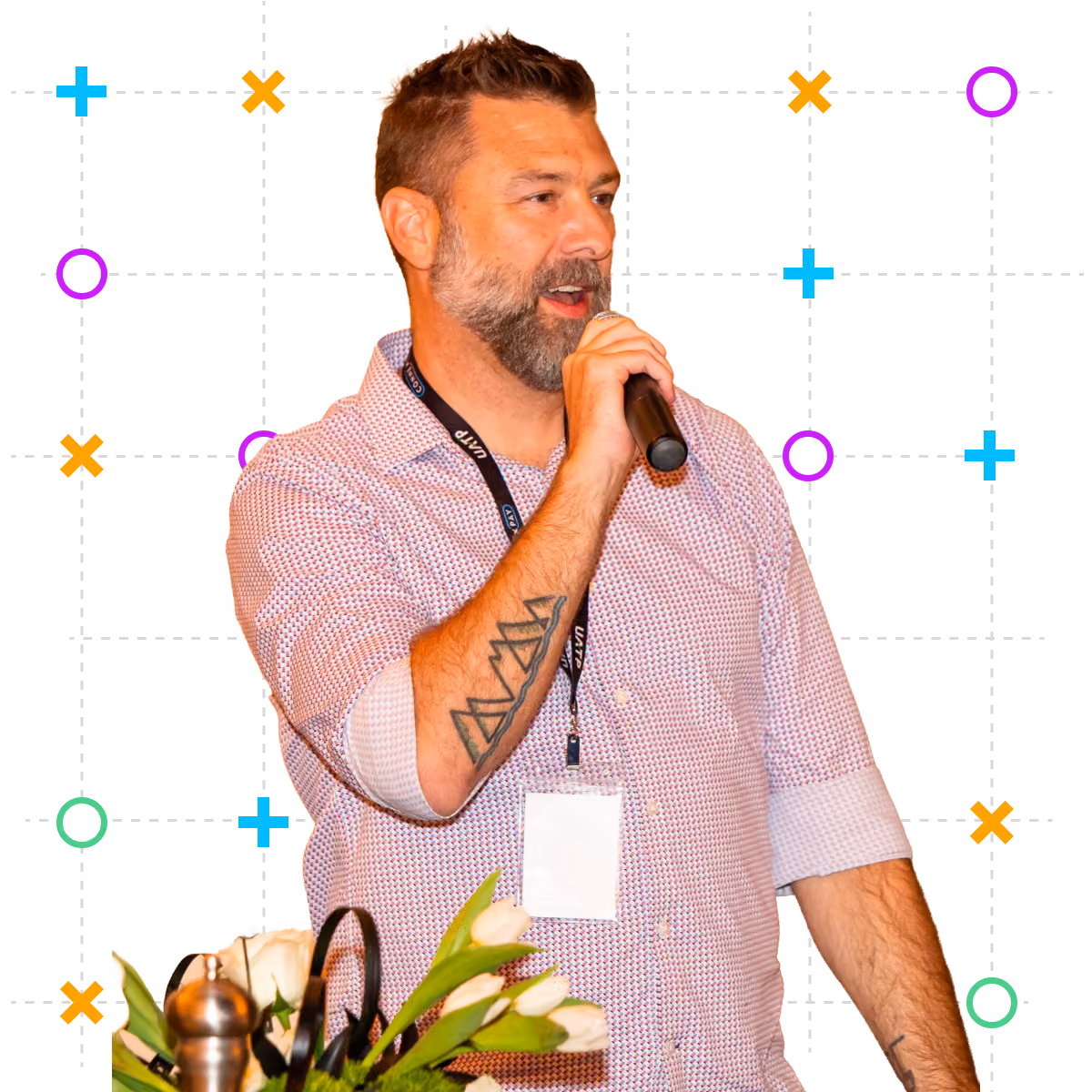 Justin at conference speaking into microphone wearing a badge and patterned shirt.