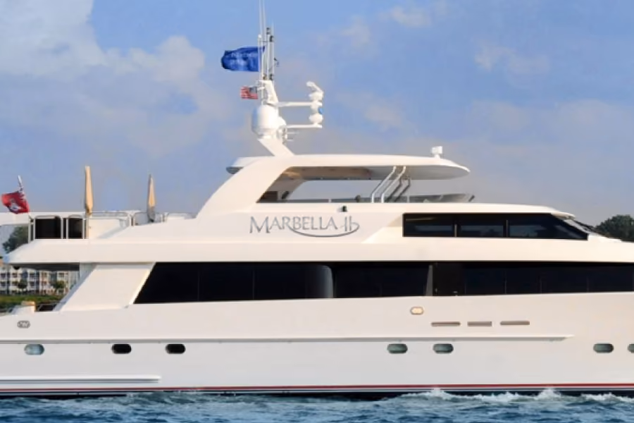 White luxury yacht named Marbella 1b on water with flags and a clear sky background.