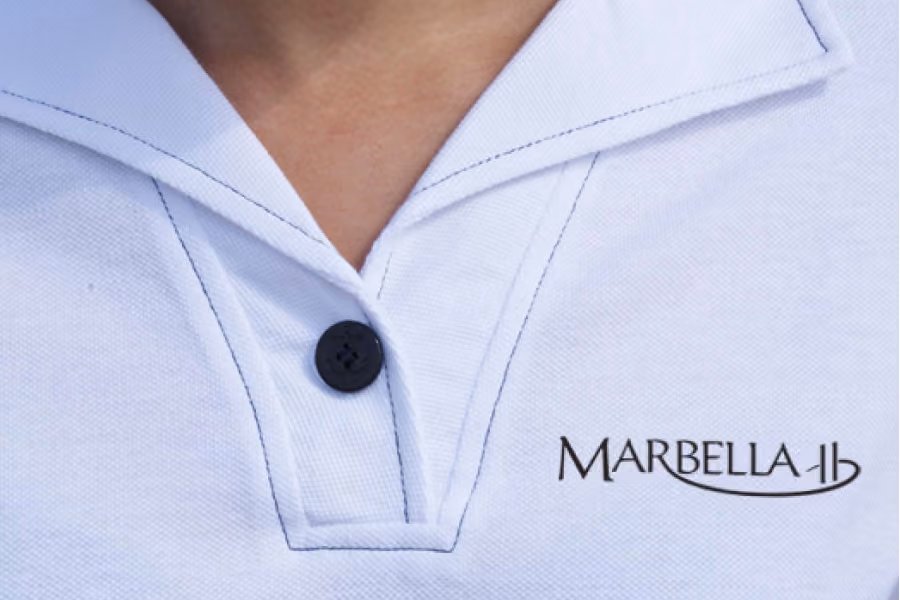 Close-up of a white collared shirt with a black button and Marbella logo on the chest.