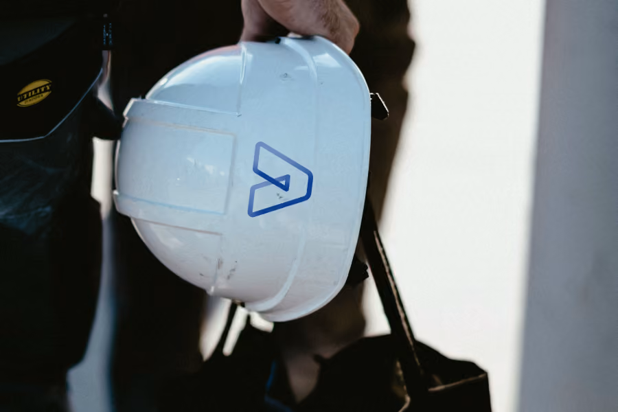 Close-up of a person holding a white construction hard hat with a blue logo.