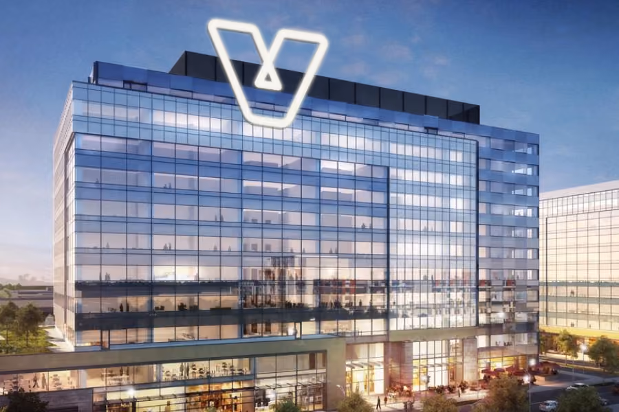Modern glass office building at dusk with illuminated V-shaped logo on top.