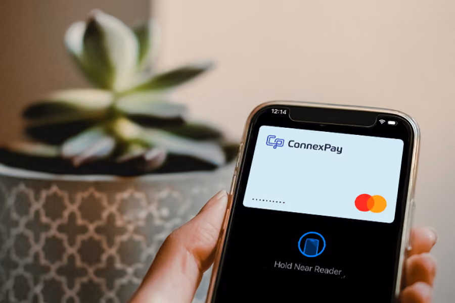 Hand holding smartphone showing a digital ConnexPay Mastercard for contactless payment.