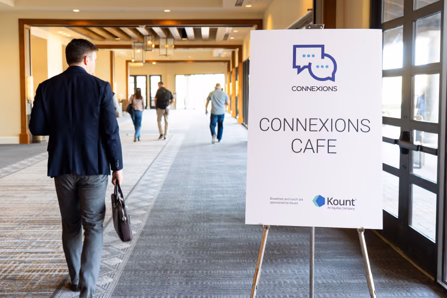 Sign for Connexions Cafe with logo and sponsorship by Kount in a hallway with people walking away.