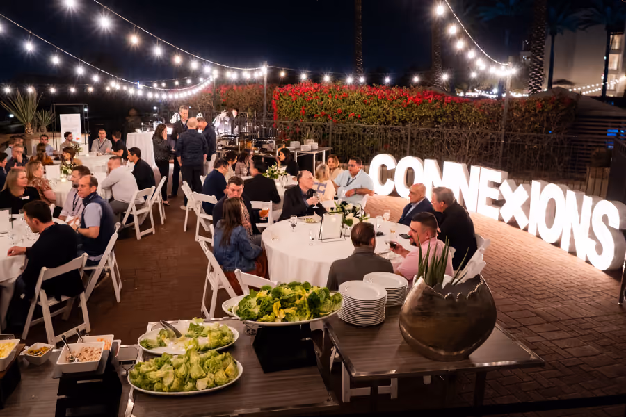 People dining at outdoor tables under string lights next to large illuminated letters spelling CONNEXIONS.