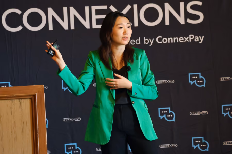 Woman in green blazer giving a presentation in front of a Connexions by ConnexPay backdrop.