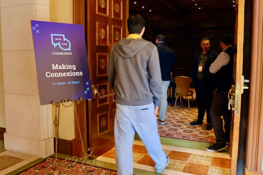 Person walking toward room with three others inside near a sign reading Making Connexions 11:30am–12:30pm.