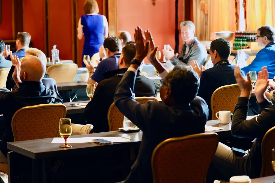 Audience seated at tables applauding a speaker in a conference room.