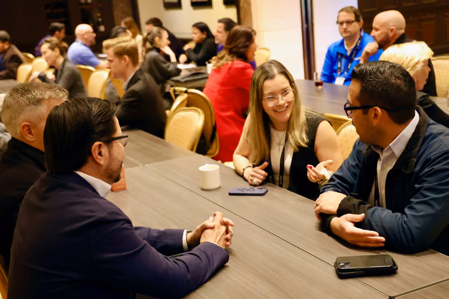 People in business attire engaged in conversation around tables at a networking event or meeting.