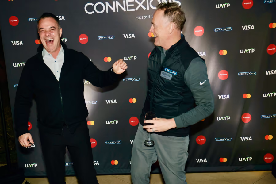 Two men laughing and fist bumping at an event with Connexions and Visa logos in the background.