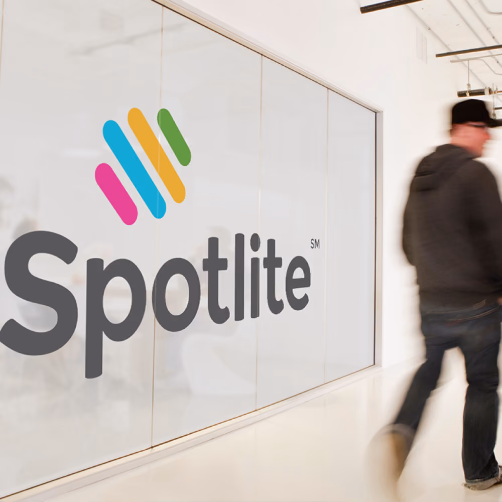 Person walking past a glass wall with a colorful Spotlite logo inside an office.