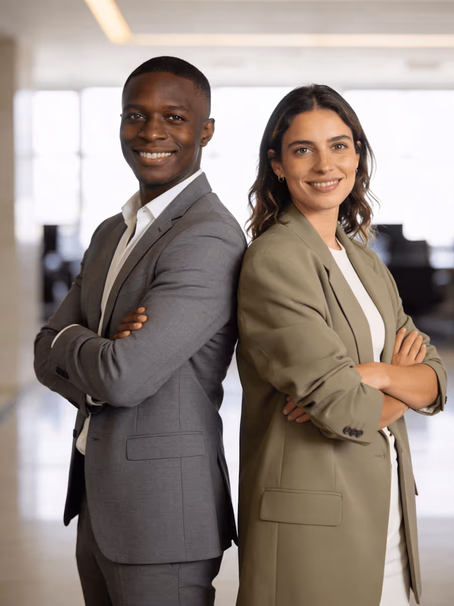Two confident professionals standing back to back with arms crossed, smiling in an office setting.