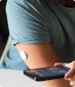 Person scanning a continuous glucose monitor sensor on arm with smartphone for metabolic tracking