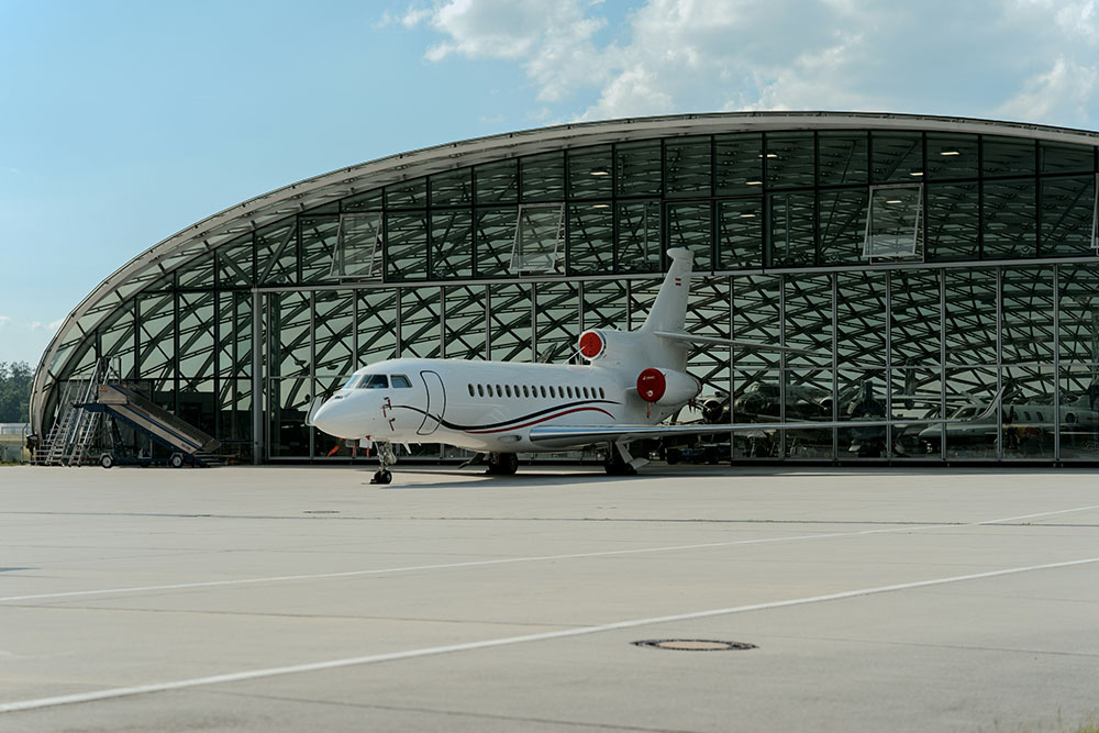 A white private jet is parked in front of a hangar,