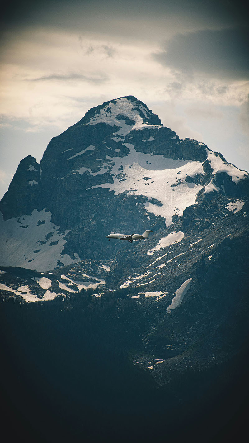 A private jet charter fly's in front of majestic snow capped mountains