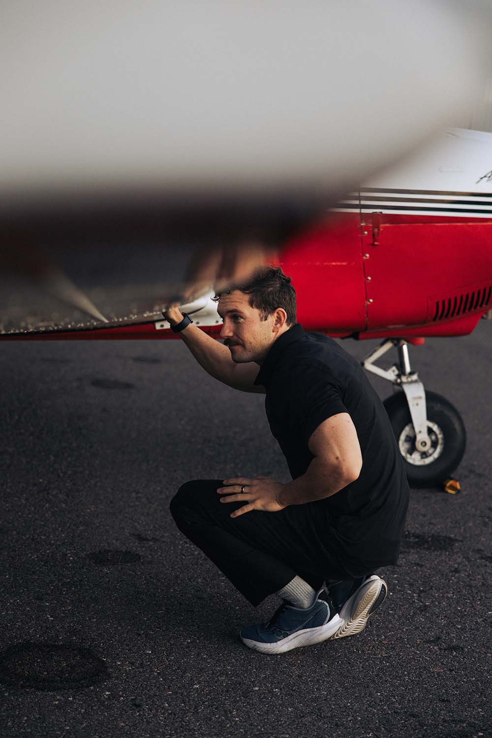 A man kneels under the wing of a private jet.