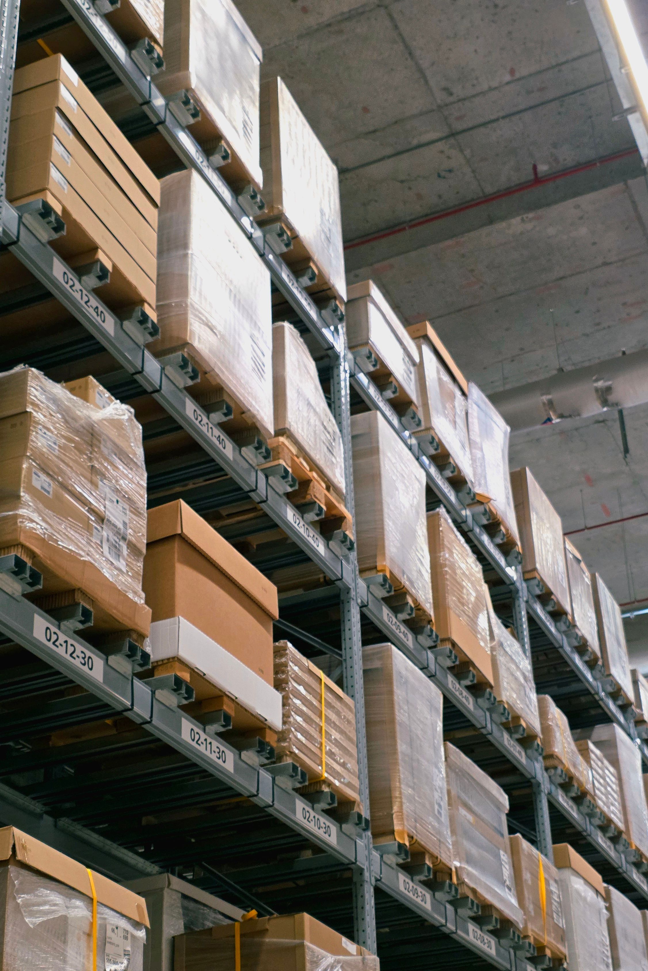 Warehouse shelves stacked high with cardboard boxes and pallets wrapped in plastic.