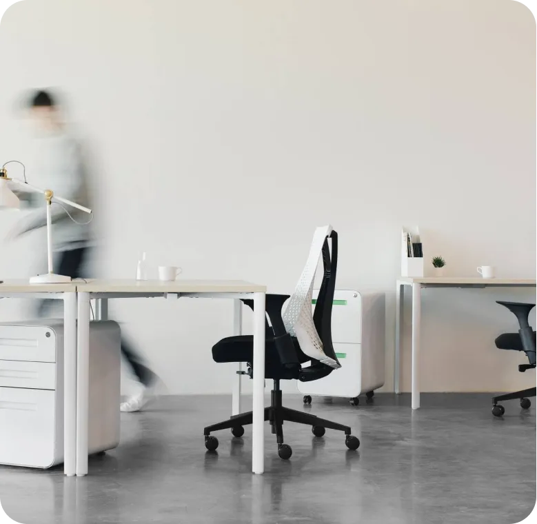 Modern minimalist office with white desks, black ergonomic chairs, and a blurred person walking.