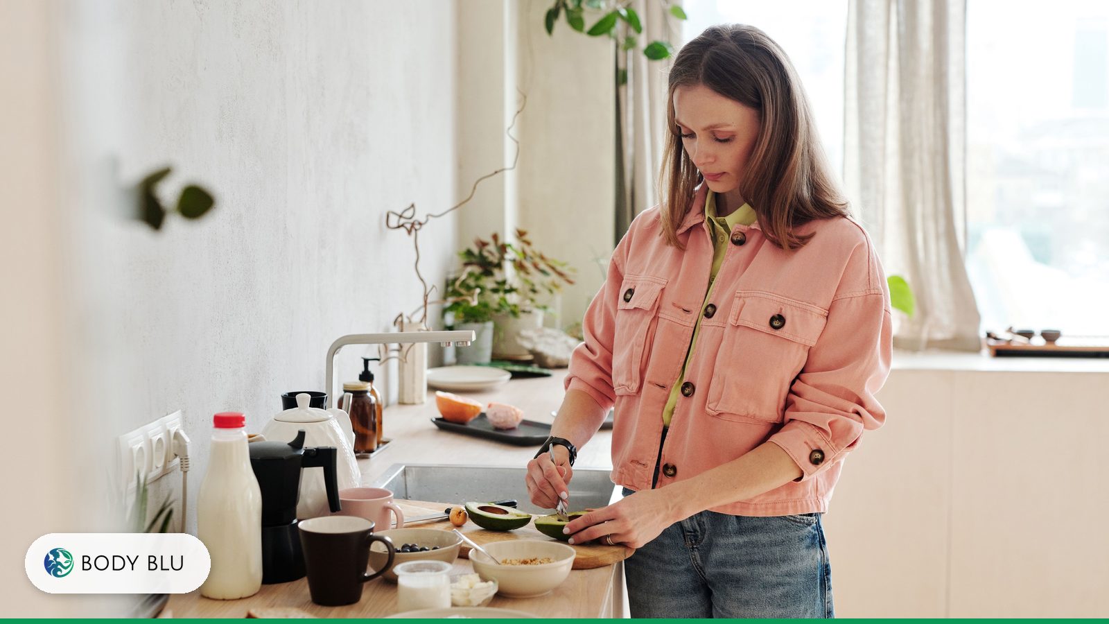 Woman in a pink jacket slicing avocado in a bright kitchen while preparing a healthy breakfast for insulin resistance