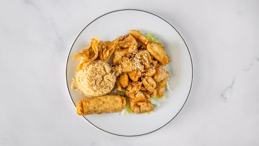 Plate of teriyaki chicken with sesame seeds, fried rice, egg roll, and wonton chips on white surface.