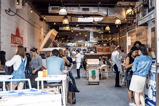 Interior of an indoor food market with string lights, food stalls, and people dining and browsing