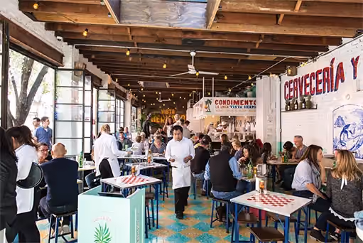 Busy open-air restaurant with tiled floors, wood beams, and a chef walking between tables of diners