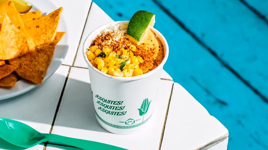 Corn esquites in a cup, topped with cotija cheese, morita mayo, chile powder and lime