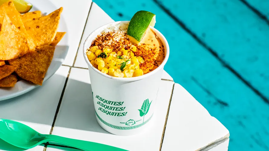 Corn esquites in a cup, topped with cotija cheese, morita mayo, chile powder and lime