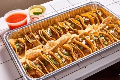 A tray of 30 carnitas tacos with tender, crispy pork, served with crunchy chicharrón and bright orange habanero salsa—perfect for sharing.