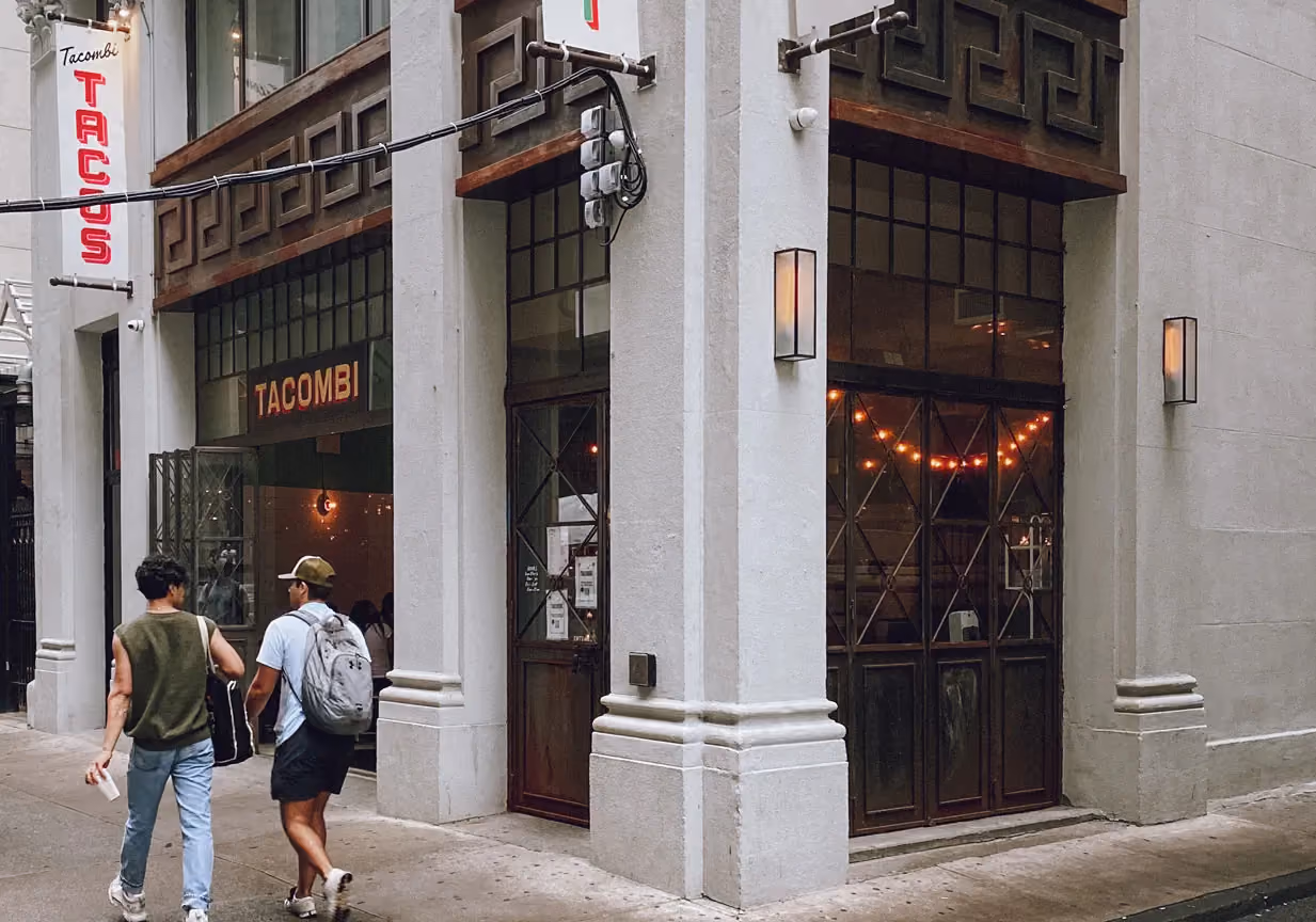 Exterior storefront of Tacombi restaurant on a city street corner, with pedestrians walking past