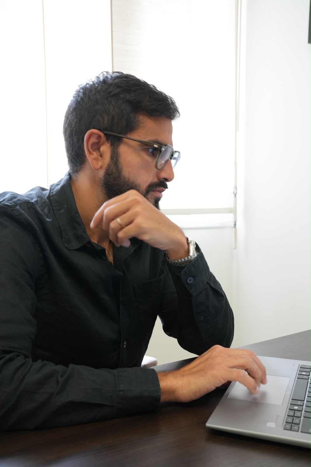 Un homme portant des lunettes et une chemise noire utilise un ordinateur portable à une table.