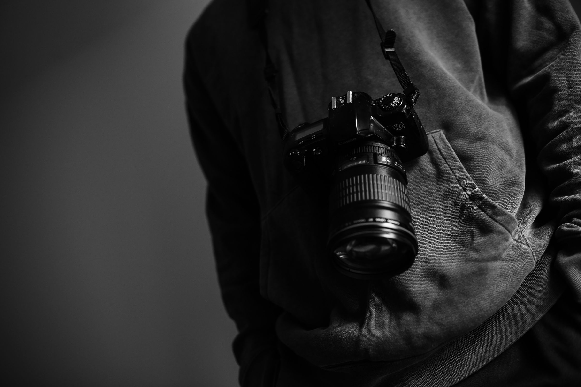 Person wearing a dark hoodie with a Canon EOS 500 camera hanging from their neck.