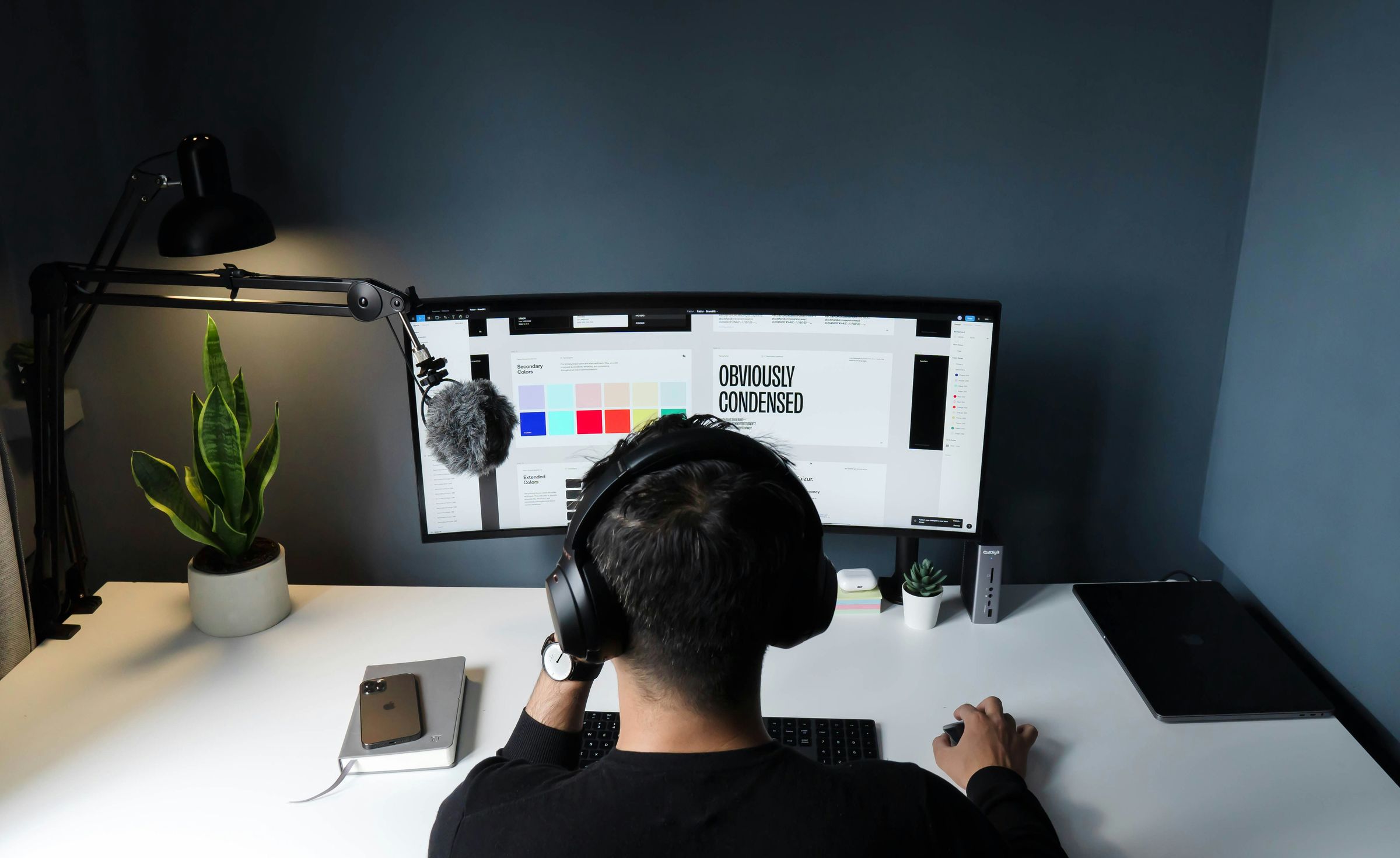 Person with headphones working on a large curved monitor displaying color swatches and text.