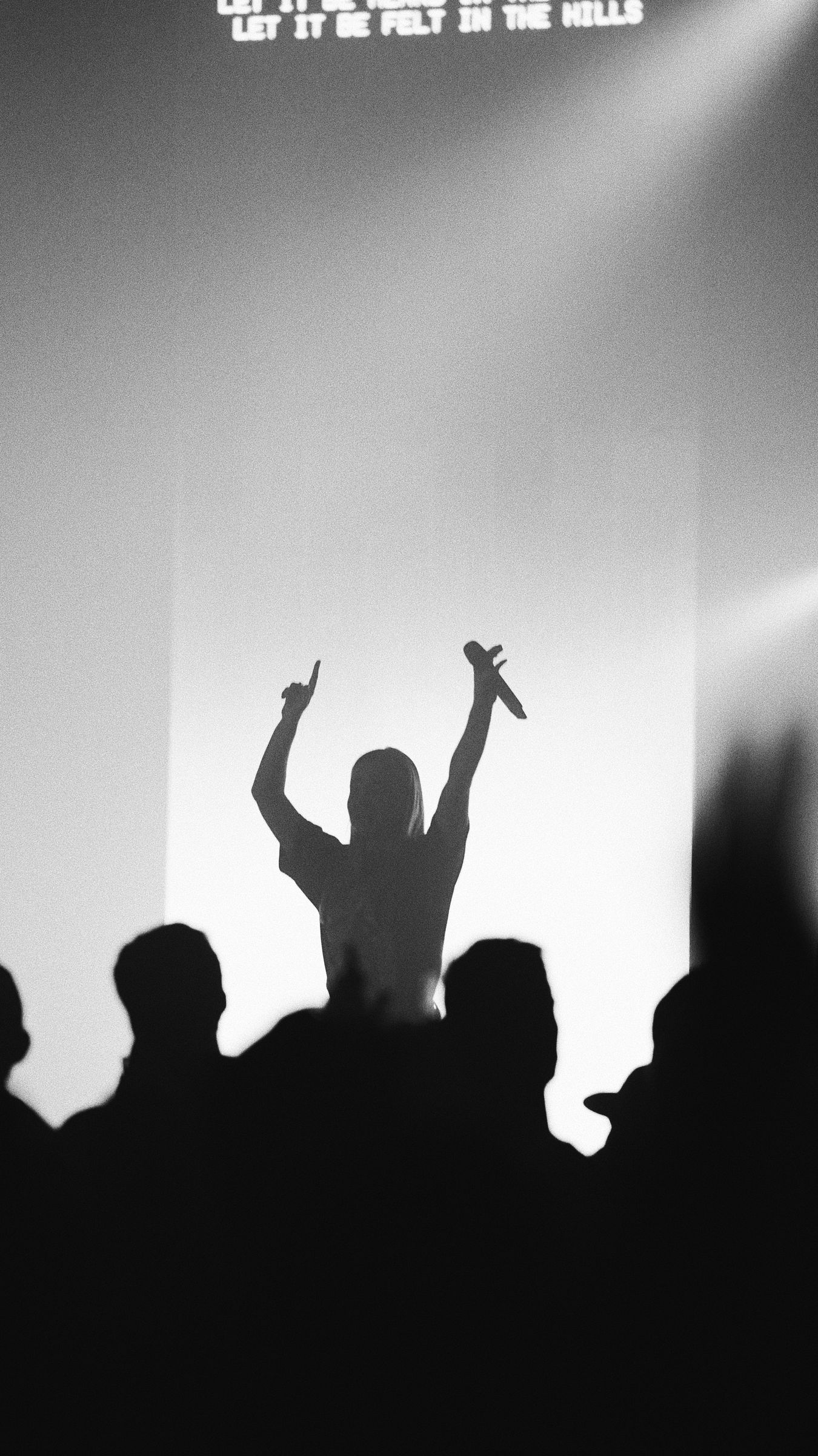 Silhouette of a performer holding a microphone with raised arms in front of an audience in black and white.