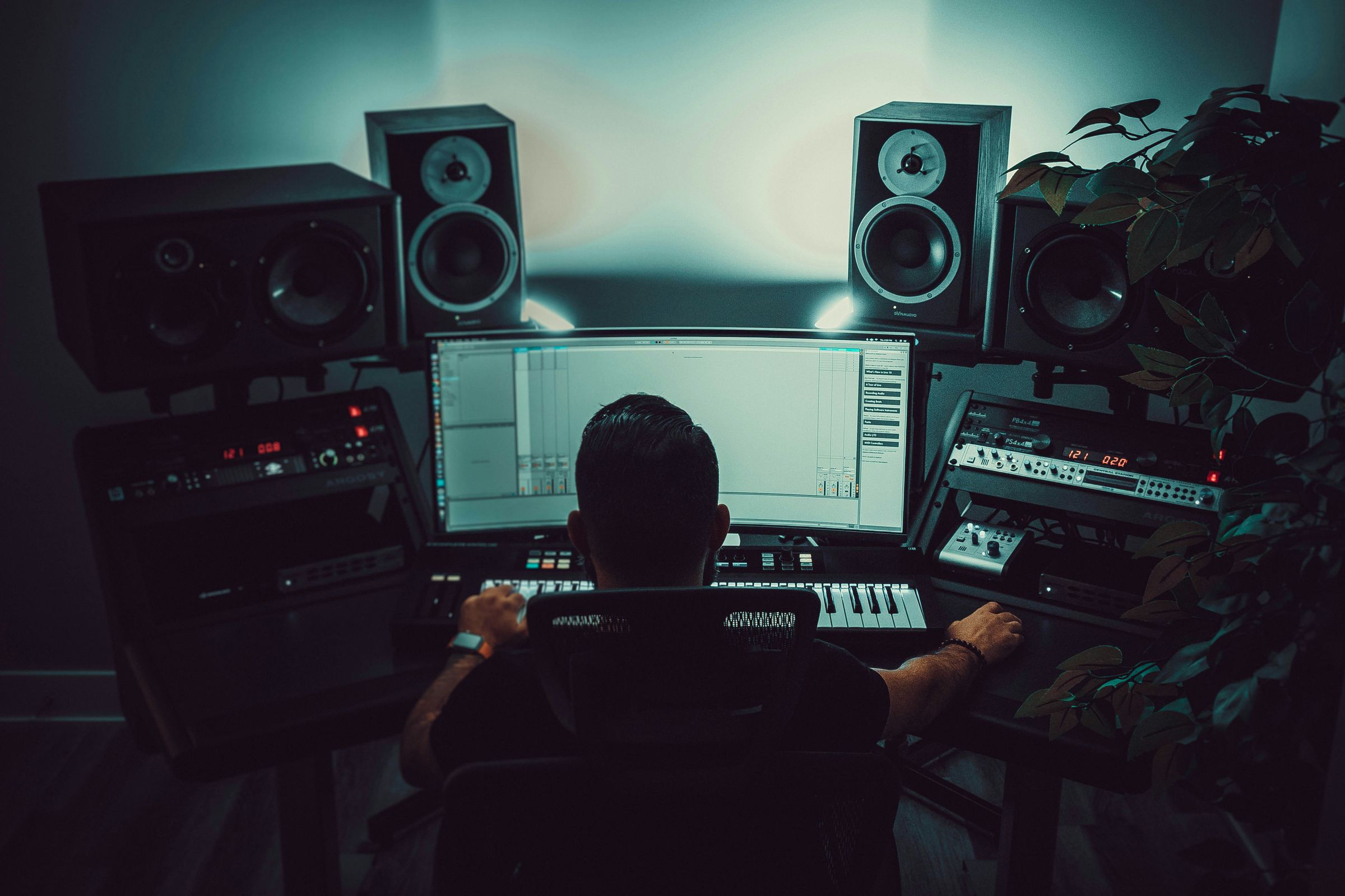 Person assis devant un écran large dans un studio avec clavier MIDI et enceintes audio.