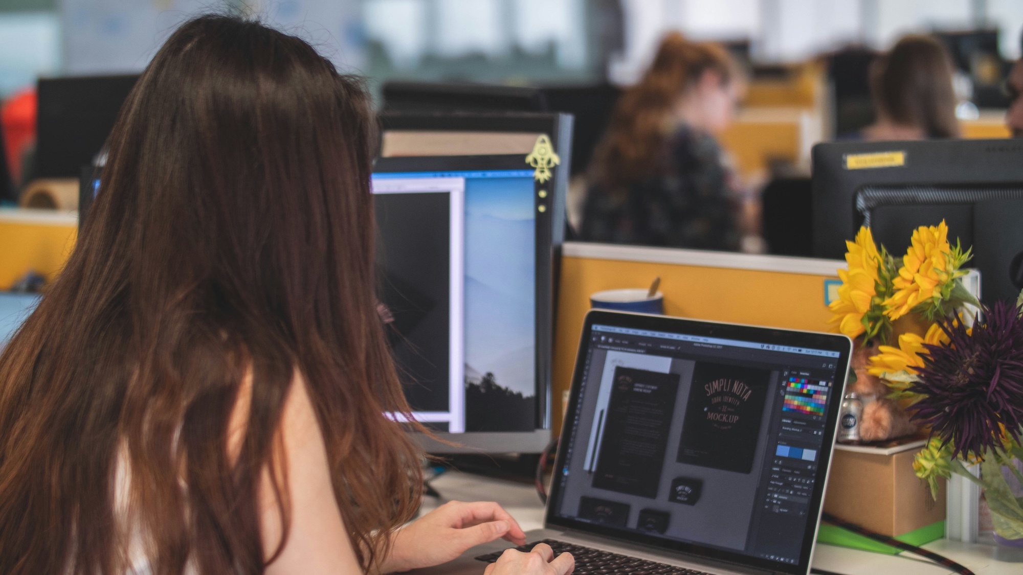 Une femme travaille sur un ordinateur portable avec un logiciel de design graphique dans un bureau.