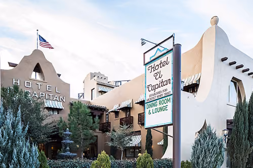 Exterior of Hotel El Capitan with Southwestern architecture, American flag, and a sign for dining room and lounge.