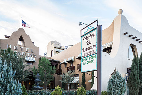 Exterior of Hotel El Capitan with Southwestern architecture, American flag, and a sign for dining room and lounge.
