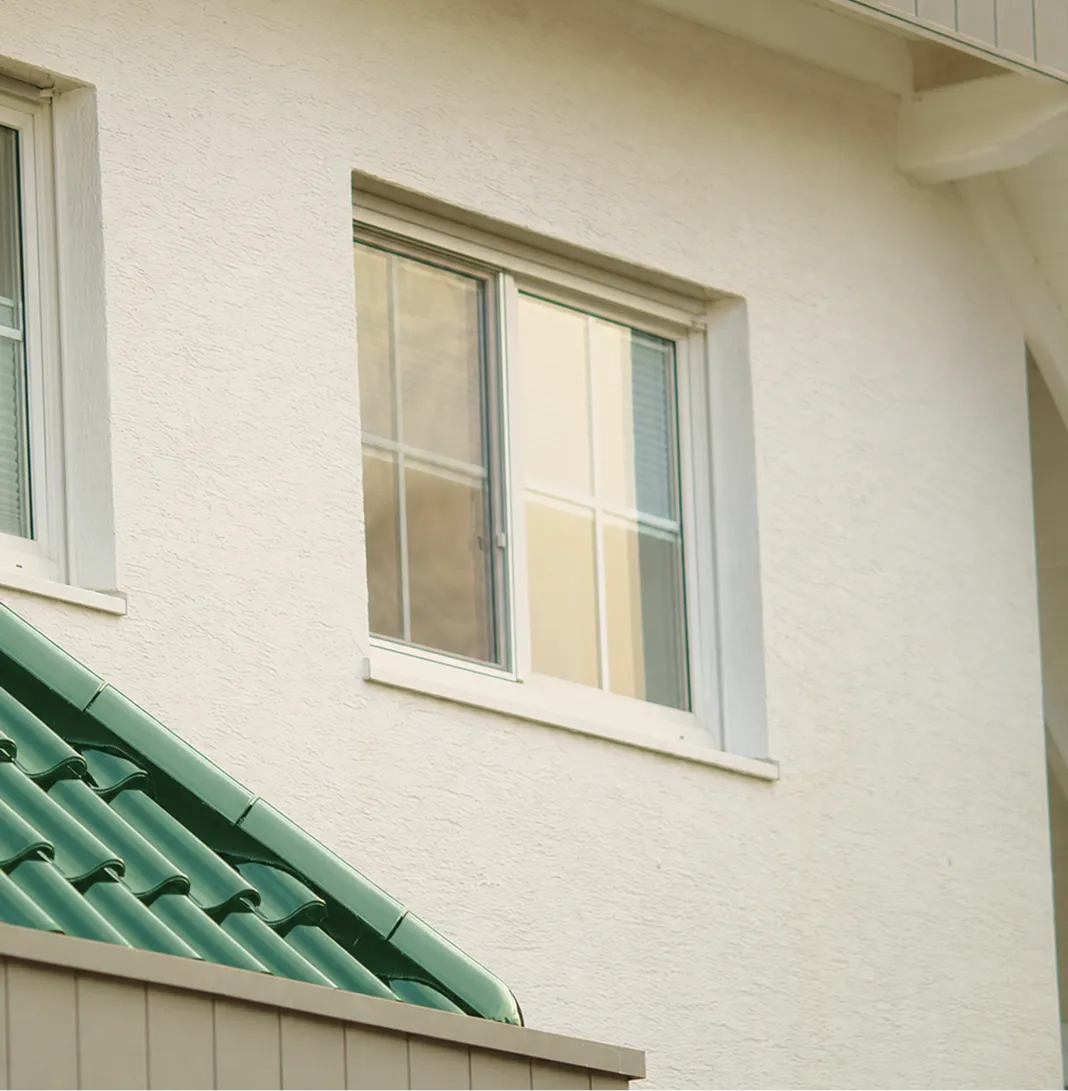 White exterior wall with two windows and a green tiled roof section below the windows.