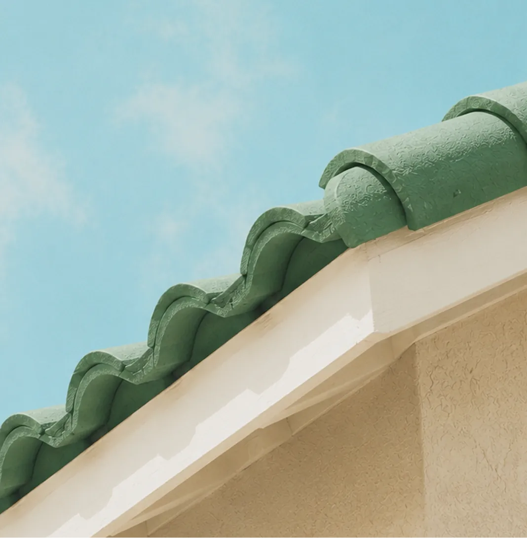 Close-up of green curved roof tiles on a beige stucco building under a clear blue sky.