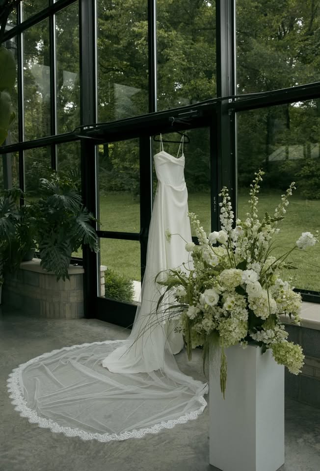 Bride and groom sharing a kiss under a veil in front of a white church with trees around.