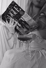 A woman in gloves holding a glass of wine and an issue of Vogue magazine.