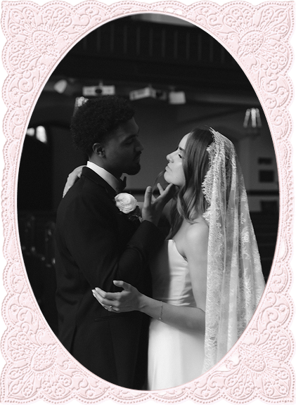 Black and white photo of a bride in a veil and groom in a suit embracing and about to kiss.